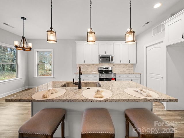 kitchen featuring visible vents, a sink, a kitchen breakfast bar, stainless steel appliances, and decorative backsplash