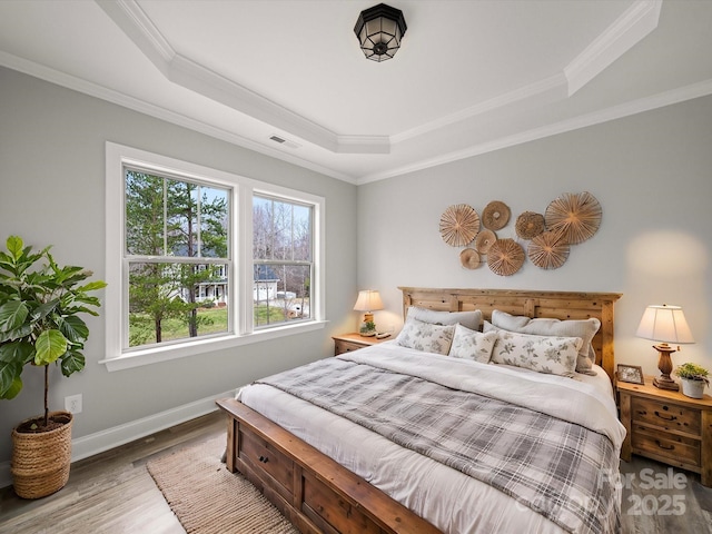 bedroom featuring visible vents, a raised ceiling, wood finished floors, crown molding, and baseboards