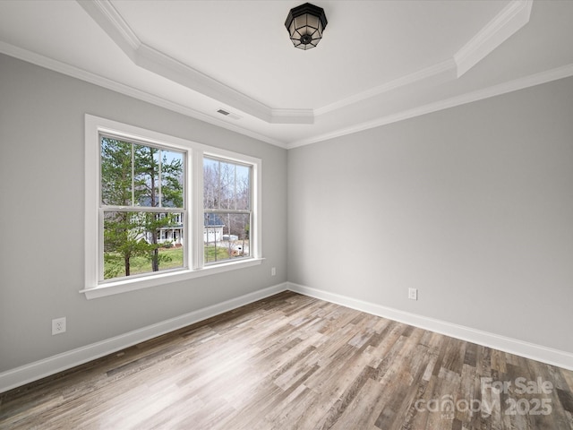 empty room featuring ornamental molding, baseboards, a tray ceiling, and wood finished floors