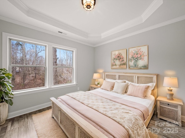 bedroom with a raised ceiling, crown molding, wood finished floors, and baseboards