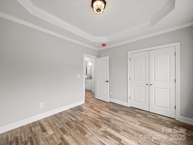 unfurnished bedroom featuring ornamental molding, a tray ceiling, wood finished floors, a closet, and baseboards