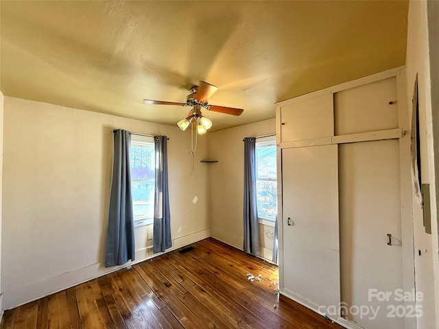 unfurnished bedroom with baseboards, multiple windows, visible vents, and dark wood-type flooring