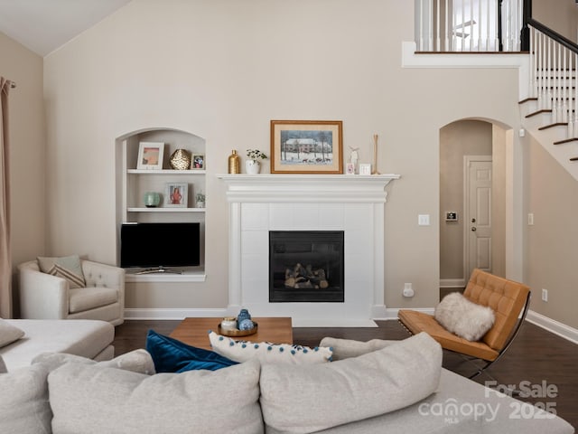 living area featuring a fireplace, built in shelves, dark wood-style floors, and high vaulted ceiling