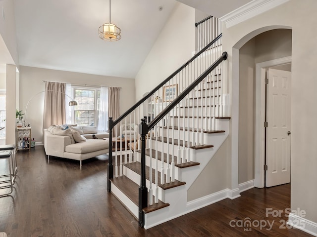 staircase featuring arched walkways, high vaulted ceiling, baseboards, and wood finished floors