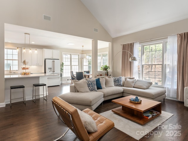 living area featuring high vaulted ceiling, a healthy amount of sunlight, dark wood-type flooring, and visible vents
