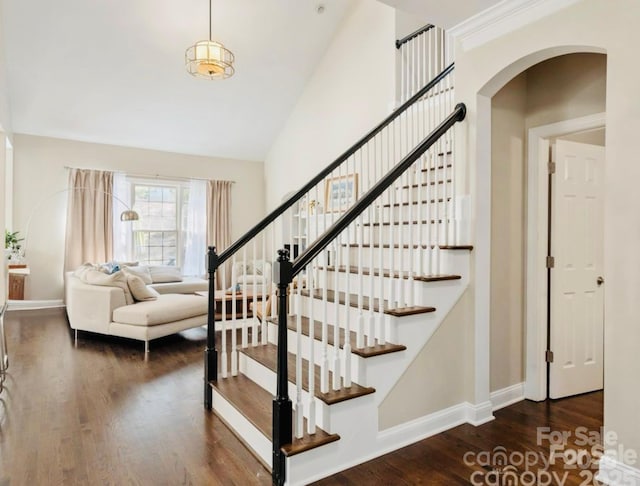 stairway with a high ceiling, wood finished floors, baseboards, and arched walkways