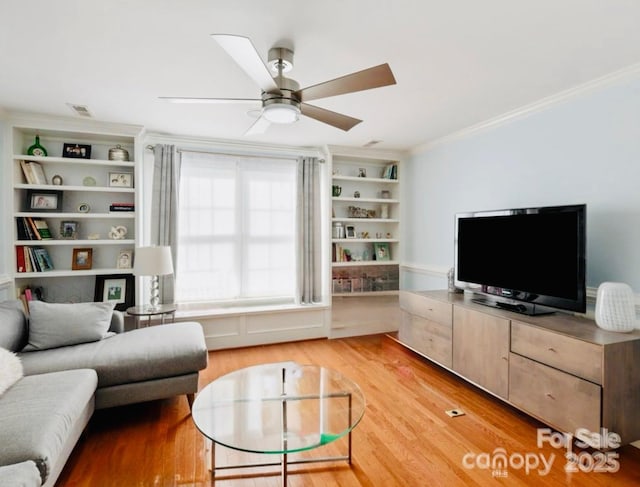 living room featuring ceiling fan, built in features, light wood finished floors, ornamental molding, and visible vents