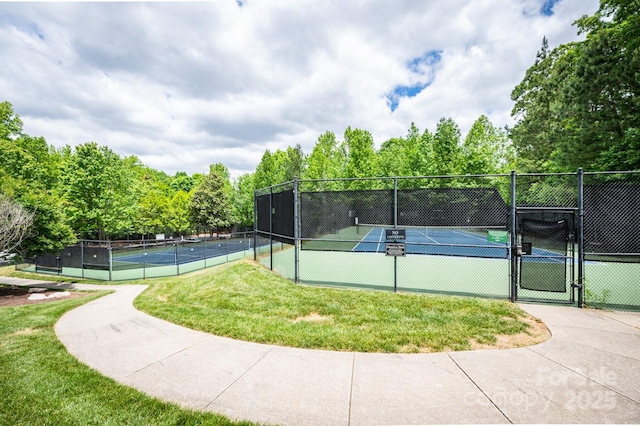 view of tennis court with fence, a lawn, and a gate