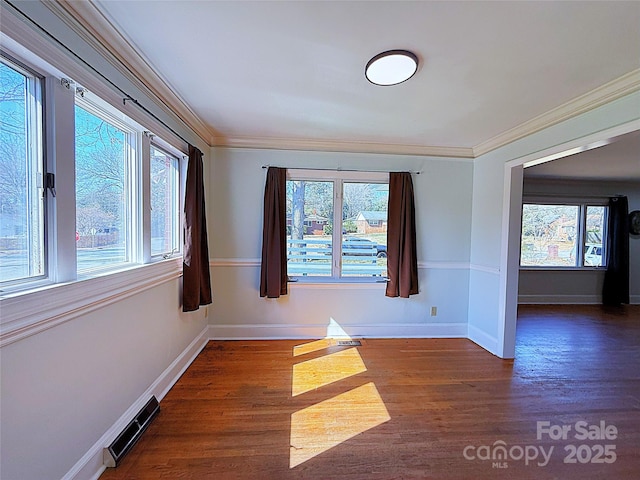 empty room featuring ornamental molding, visible vents, baseboards, and wood finished floors