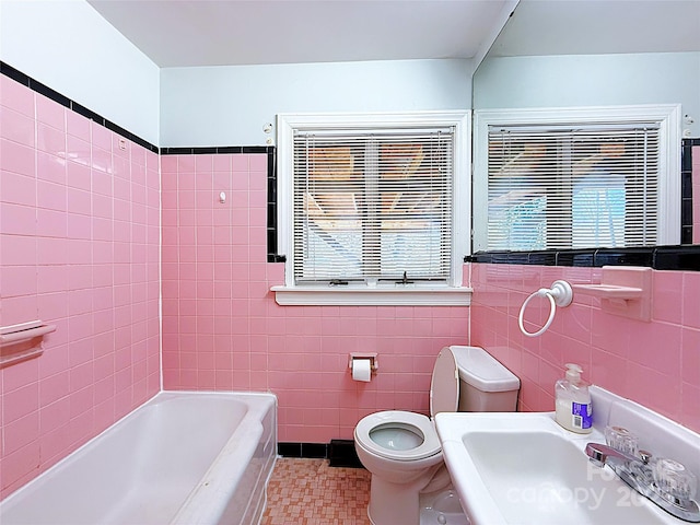 full bath featuring a tub to relax in, a sink, tile walls, and toilet