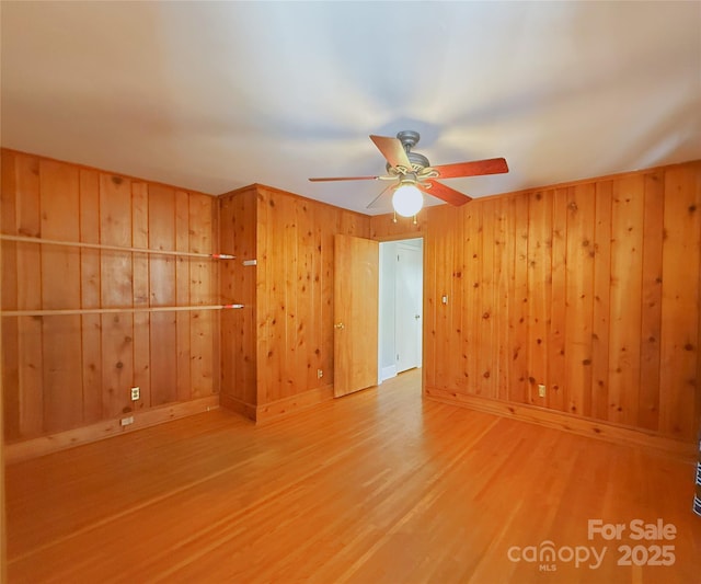 empty room with ceiling fan, wooden walls, baseboards, and wood finished floors