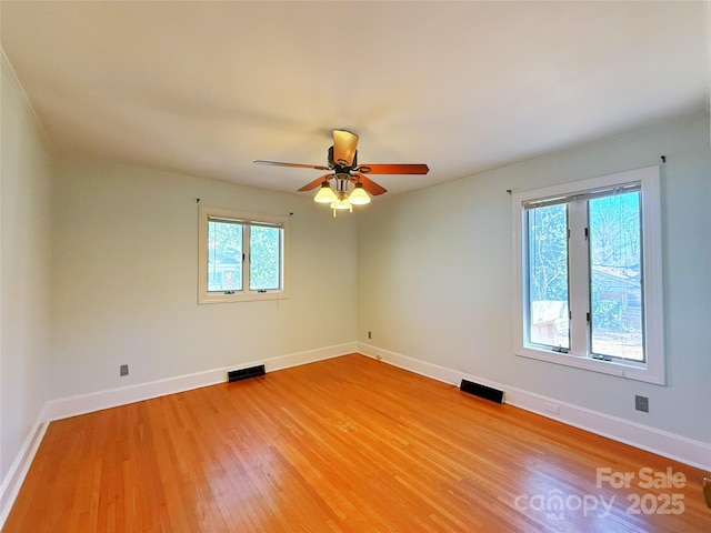 empty room with light wood finished floors, visible vents, and baseboards