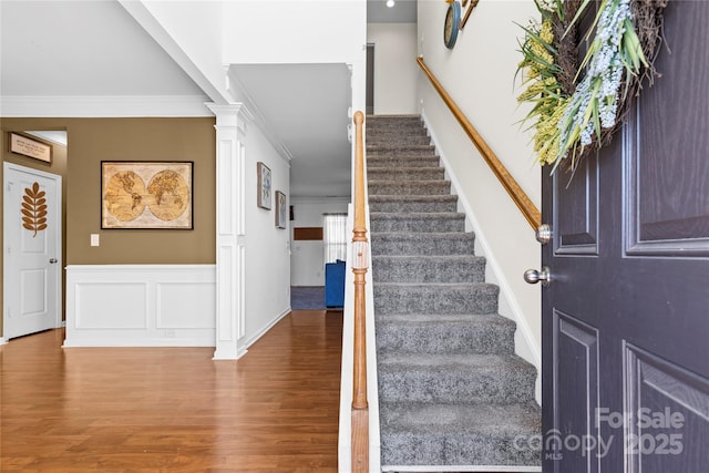 entryway with decorative columns, stairway, ornamental molding, wood finished floors, and a decorative wall