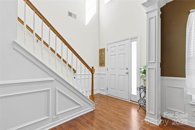 entryway with a decorative wall, wood finished floors, visible vents, stairs, and decorative columns