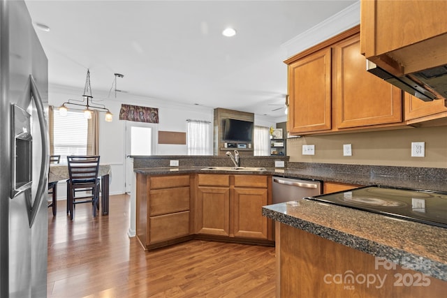 kitchen with stainless steel appliances, brown cabinetry, a sink, and a peninsula