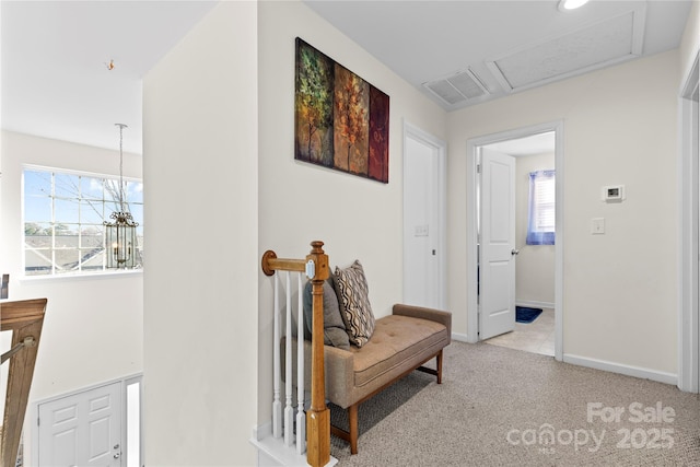 corridor with a notable chandelier, light carpet, visible vents, baseboards, and attic access