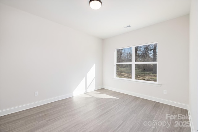 spare room with wood finished floors, visible vents, and baseboards