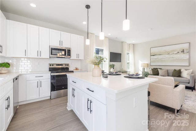 kitchen featuring a center island, open floor plan, decorative backsplash, light wood-style flooring, and appliances with stainless steel finishes