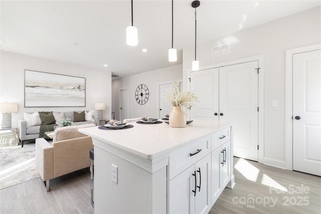 kitchen with white cabinetry, visible vents, light wood-type flooring, and a kitchen island