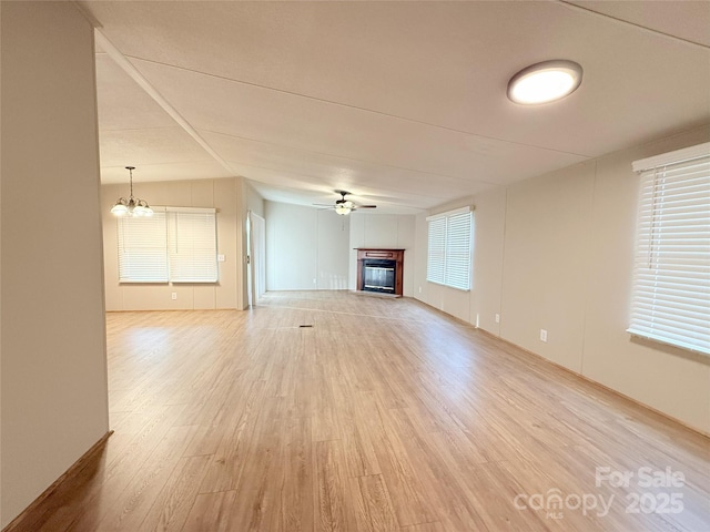 unfurnished living room featuring light wood-style floors, a glass covered fireplace, and ceiling fan with notable chandelier