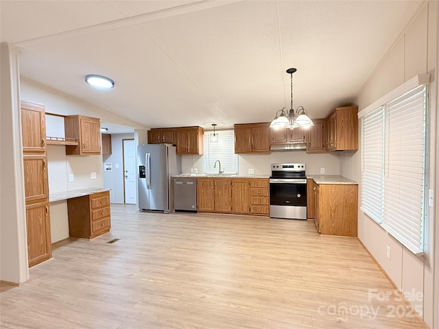 kitchen with light wood finished floors, appliances with stainless steel finishes, brown cabinets, vaulted ceiling, and light countertops