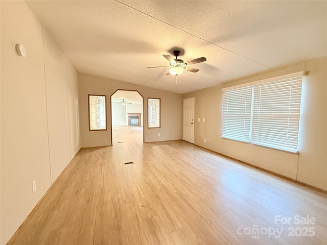 unfurnished room featuring light wood-style floors, ceiling fan, arched walkways, and a textured ceiling