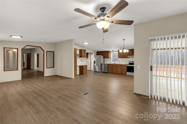 unfurnished living room featuring ceiling fan with notable chandelier, lofted ceiling, visible vents, and dark wood-type flooring