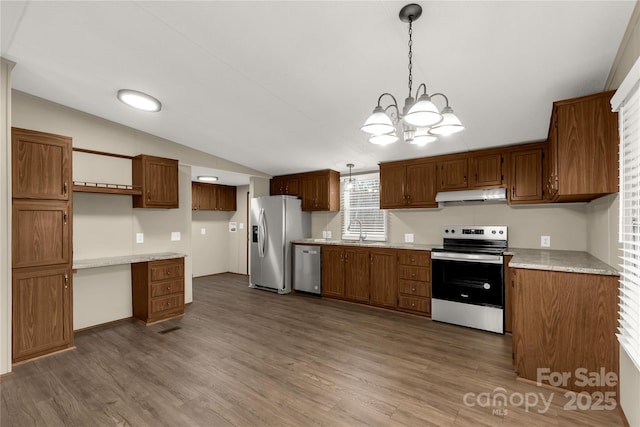 kitchen with a sink, wood finished floors, under cabinet range hood, stainless steel appliances, and an inviting chandelier