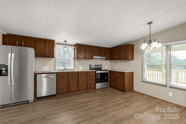 kitchen featuring light countertops, a sink, light wood-style flooring, under cabinet range hood, and stainless steel appliances