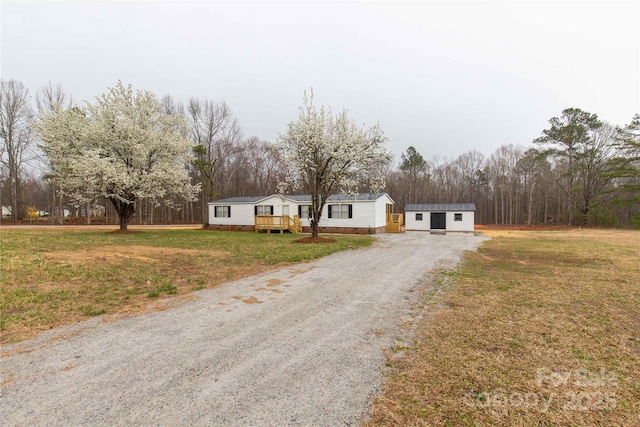 view of front of house with an outbuilding, driveway, a wooden deck, and a front lawn