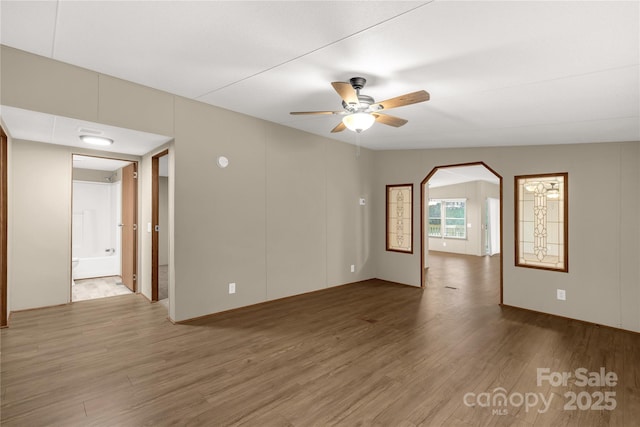 spare room featuring wood finished floors, arched walkways, and ceiling fan
