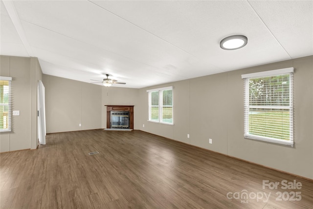 unfurnished living room featuring wood finished floors, a glass covered fireplace, and a ceiling fan