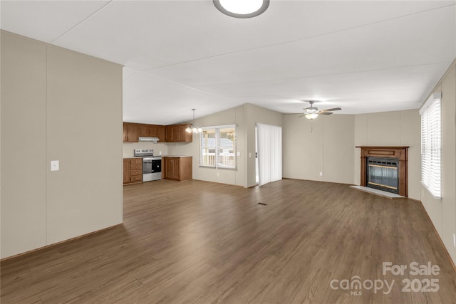 unfurnished living room featuring lofted ceiling, dark wood-style floors, a glass covered fireplace, and ceiling fan with notable chandelier
