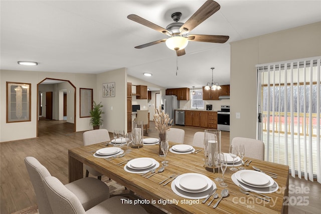 dining room with ceiling fan with notable chandelier, lofted ceiling, light wood-style floors, and arched walkways