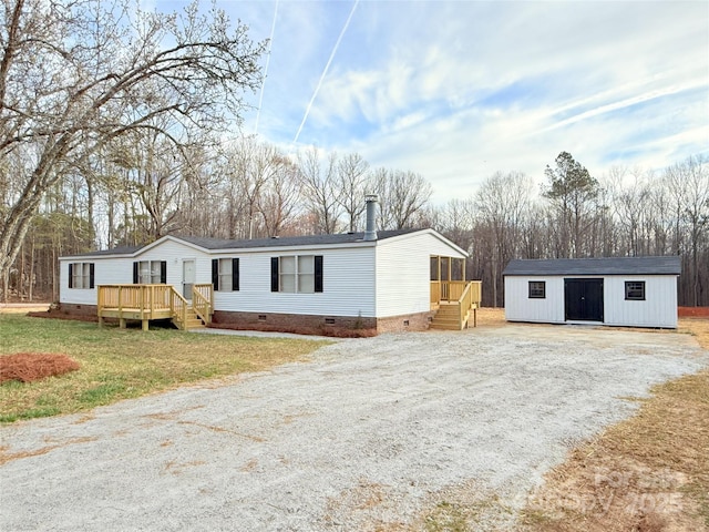 manufactured / mobile home with a wooden deck, gravel driveway, crawl space, a front lawn, and an outbuilding