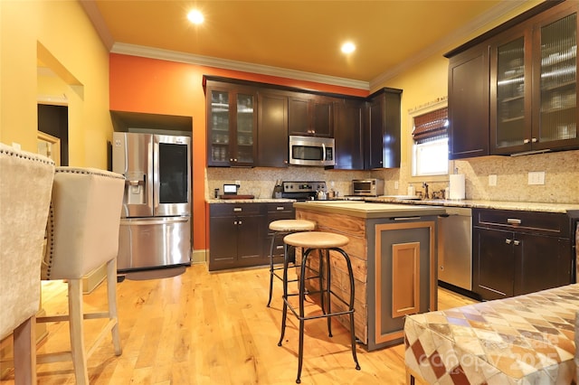 kitchen featuring crown molding, a breakfast bar area, light wood finished floors, decorative backsplash, and appliances with stainless steel finishes