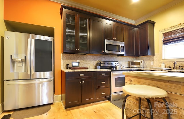 kitchen with light wood-style flooring, dark brown cabinetry, stainless steel appliances, ornamental molding, and backsplash