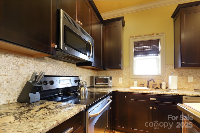 kitchen featuring dark brown cabinetry, tasteful backsplash, stainless steel appliances, crown molding, and a sink