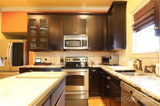 kitchen featuring dark brown cabinetry, stainless steel appliances, a sink, tasteful backsplash, and glass insert cabinets