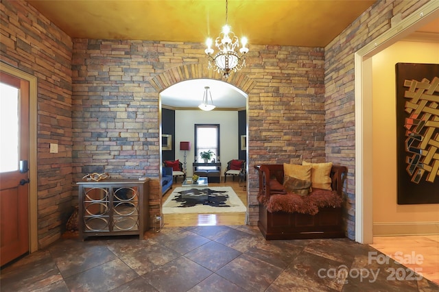 foyer entrance with baseboards, a notable chandelier, arched walkways, and stone tile flooring