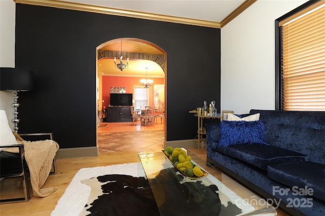 living area featuring arched walkways, baseboards, a chandelier, and crown molding