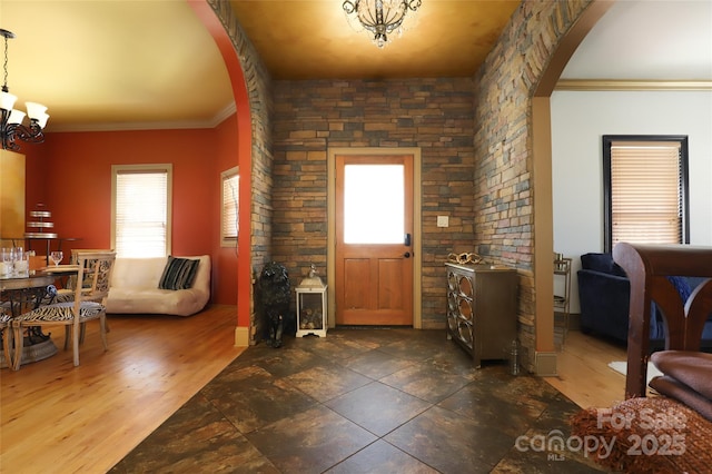 entryway with arched walkways, a chandelier, crown molding, and wood finished floors