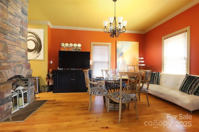 dining space featuring a chandelier, a large fireplace, crown molding, and wood finished floors