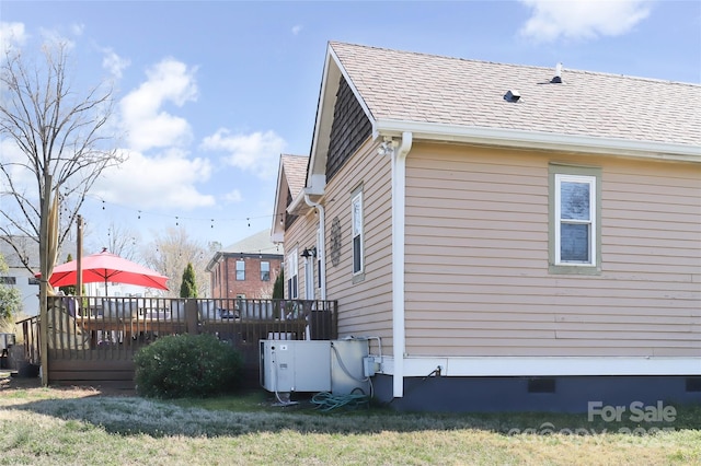 view of side of home with crawl space, a yard, a deck, and roof with shingles