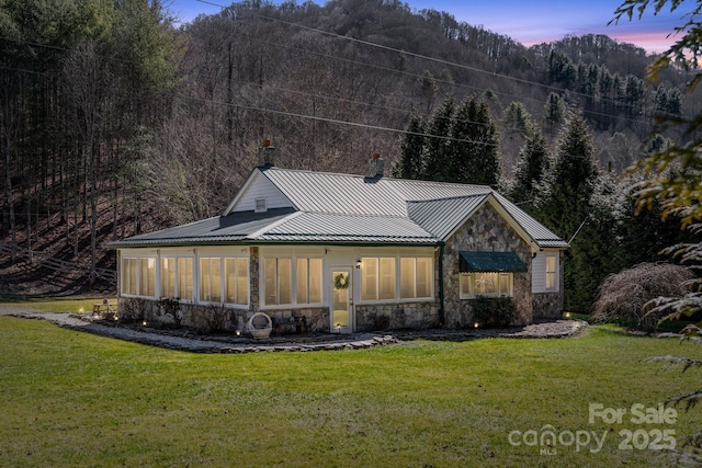 view of front of house featuring a standing seam roof, a sunroom, metal roof, stone siding, and a front lawn