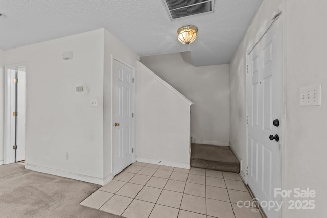 foyer featuring light tile patterned floors, visible vents, light carpet, and a textured ceiling