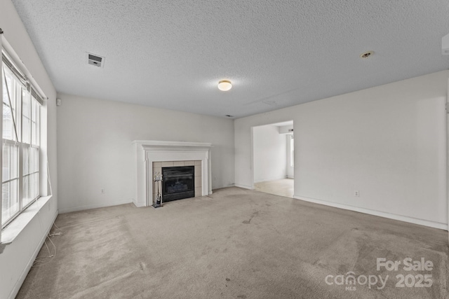 unfurnished living room featuring carpet flooring, a tile fireplace, a textured ceiling, and visible vents