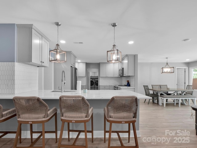 kitchen with stainless steel appliances, backsplash, light wood-style floors, a sink, and a peninsula