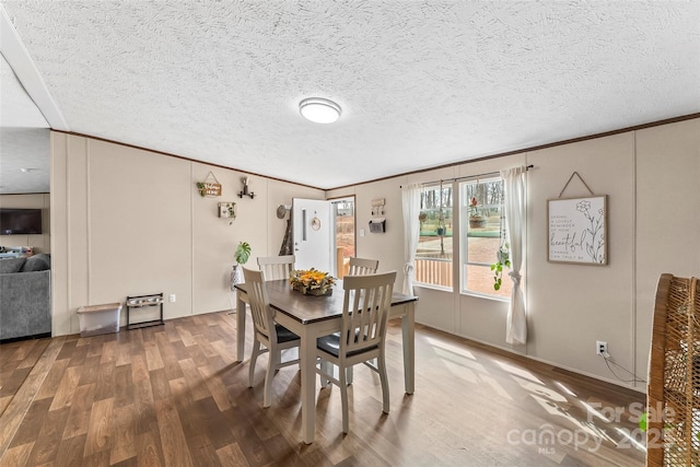 dining area featuring a textured ceiling, ornamental molding, a decorative wall, and wood finished floors