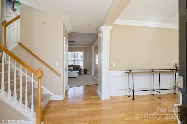 entryway featuring crown molding, light wood-style floors, stairs, and ornate columns